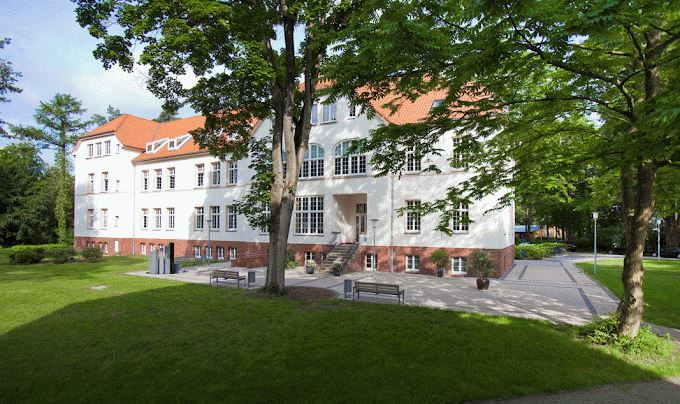 Vierstöckiges weißes Haus mit rotem Spitzdach im Park Foto der Außenstelle Gütersloh, Zentrale Akademie für Berufe im Gesundheitswesen