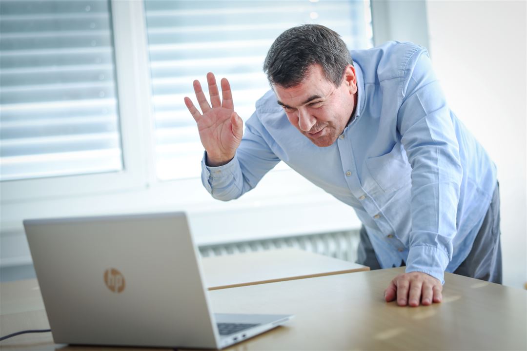 Lächelnder Mann grüßt gebückt zum Bildschirm des Laptops auf dem Tisch Foto der Außenstelle Onlinepräsenz